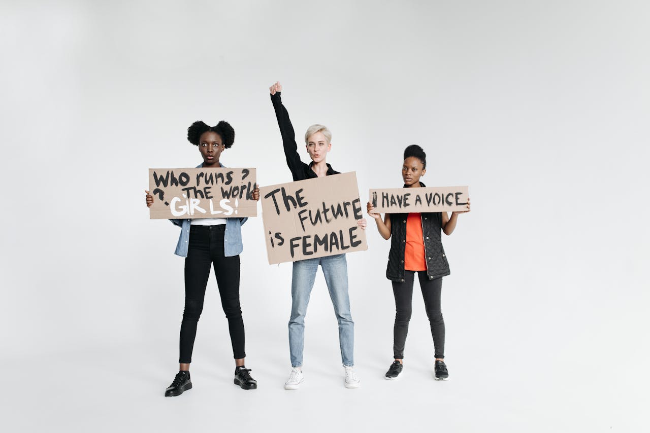 services-03 Three women holding signs advocating feminism and empowerment on a white backdrop, symbolizing unity and diversity.
